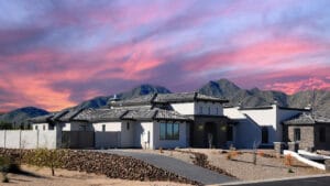 Modern home with mountain backdrop under a colorful sunset sky.