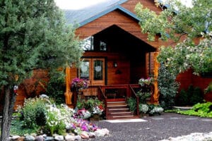 Cozy wooden cabin surrounded by lush greenery and colorful flowers.
