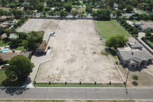 A large empty dirt lot bordered by greenery and buildings.