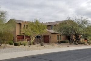 Suburban two-story house with desert landscaping and cloudy sky.